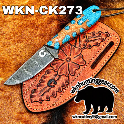 Close-up of a Damascus steel knife with a turquoise-hued handle in an orange ornamented leather sheath on brown fur.