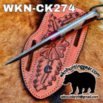 Damascus-style knife resting on a pink tooled leather sheath laid on brown horsehide, with large 'WKN-CK274' text and a black animal silhouette/logo.