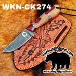 Close-up of a Damascus knife in a carved orange leather sheath on fur, with the text WNK-CK274 and a black bear logo visible.