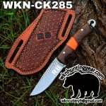 Hunting knife with a wood handle and orange wrap resting on a brown patterned leather sheath with RB branding, outdoors near grass and a tree trunk.