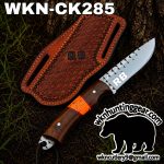 Knife with carved wooden handle and silver blade labeled 'RB', resting beside a brown leather sheath with 'RB' stamp, outdoors.
