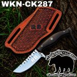 Fixed-blade knife with a dark wooden handle and a silver blade marked RB, shown with a patterned brown leather sheath outdoors on soil and grass.
