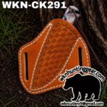 Orange leather knife sheath with white stitching on dirt, a marbled knife handle partly visible, bearing a black bear silhouette and the text 'wnkhuntinggear.com' and 'wnkcutlery9@gmail.com'
