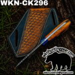 Close-up of a wooden-handled knife resting on a blue leather sheath with a tan patterned panel, outdoors; WKN-CK296 label visible.