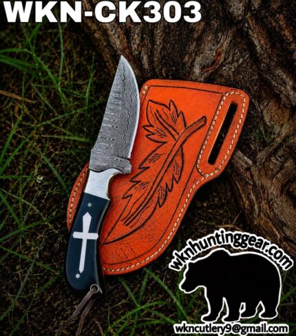Damascus fixed‑blade knife with a dark handle and cross emblem, resting beside an orange engraved leather sheath outdoors.