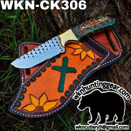 Custom knife with a patterned multicolor handle resting on an orange, sunflower-embossed leather sheath outdoors.