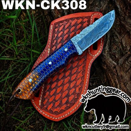 Damascus blade knife with a blue hex pattern handle laid on an orange tooled leather sheath outdoors.