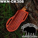 Red tooled leather knife sheath with woven pattern, tied to a tree trunk; branding text visible in corner.