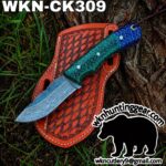 Fixed-blade knife with Damascus-pattern blade and green hexagonal-scale handle on an orange leather sheath outdoors.