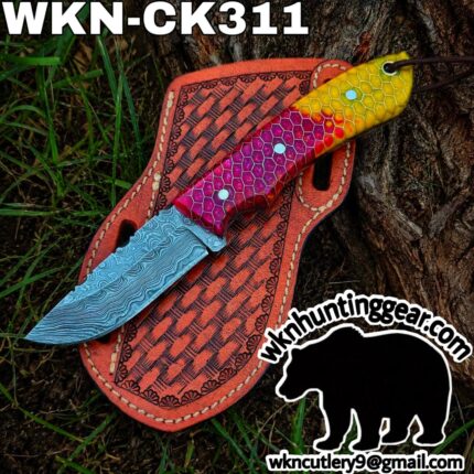 Multicolor fixed‑blade knife with a blue Damascus-pattern blade and a bright, honeycomb‑pattern handle laid on a red leather sheath outdoors.
