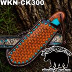 Leather knife sheath with orange-brown patterned panels, turquoise studs, and a wooden knife handle partially visible against a tree.