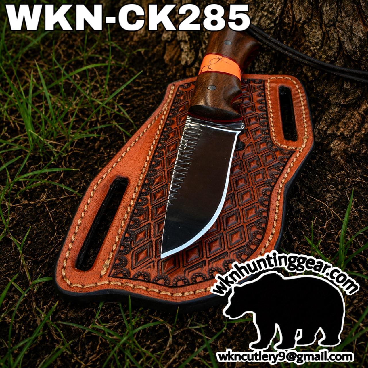 Fixed-blade knife with wooden handle in a brown embossed leather sheath on soil, text WKNC K285 at top edge.