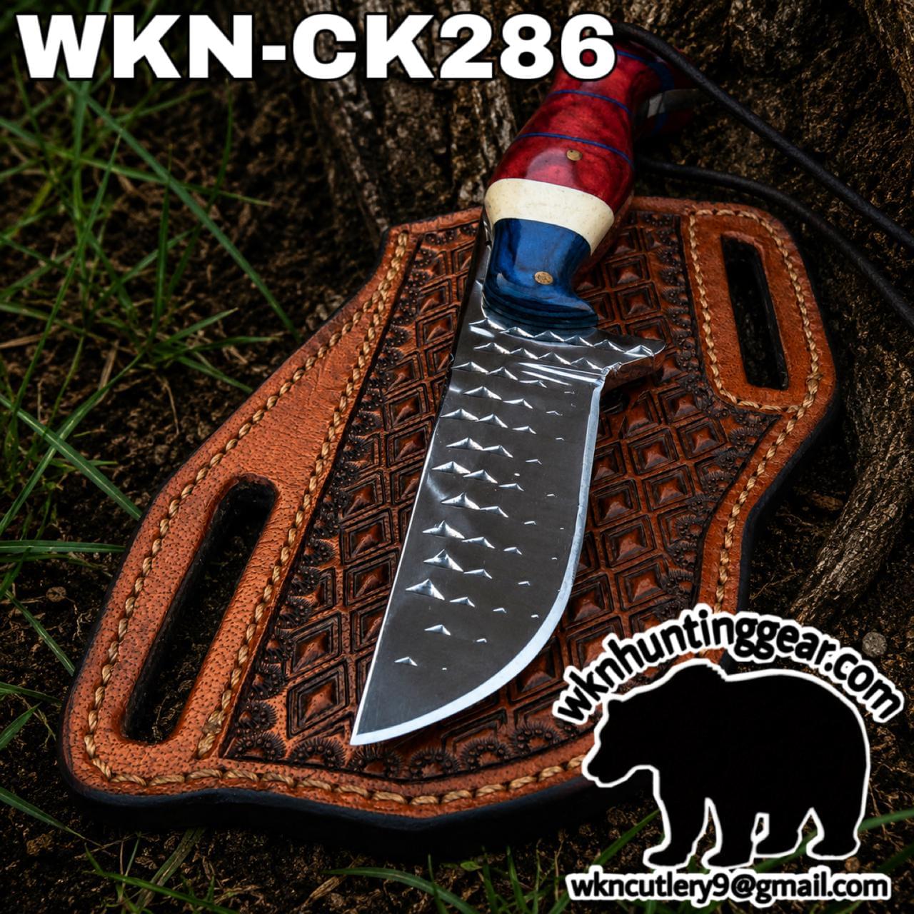 Fixed-blade knife with a hammered silver blade on a brown tooled leather sheath outdoors.