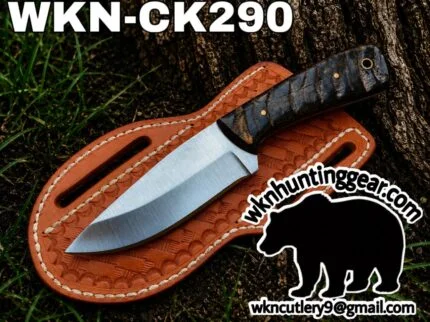 Fixed-blade knife with textured handle laid on a brown leather sheath outdoors; branding text WKN-CK290 appears above.