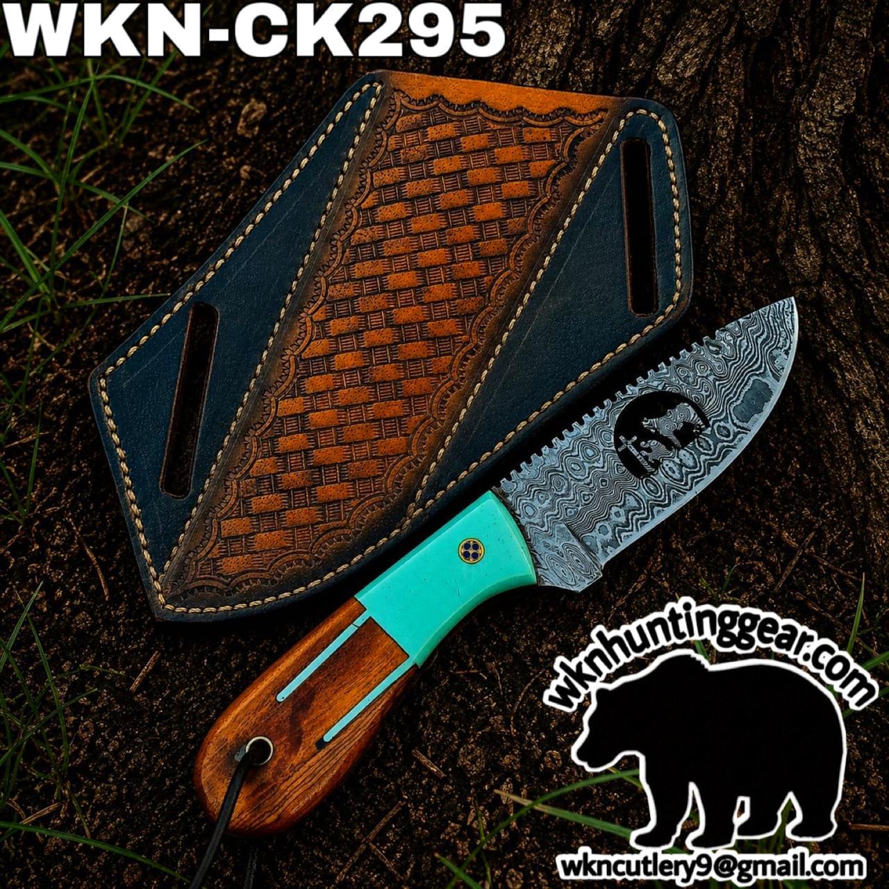 Knife with a patterned Damascus blade and turquoise handle lying on dirt beside a decorative leather sheath or case.