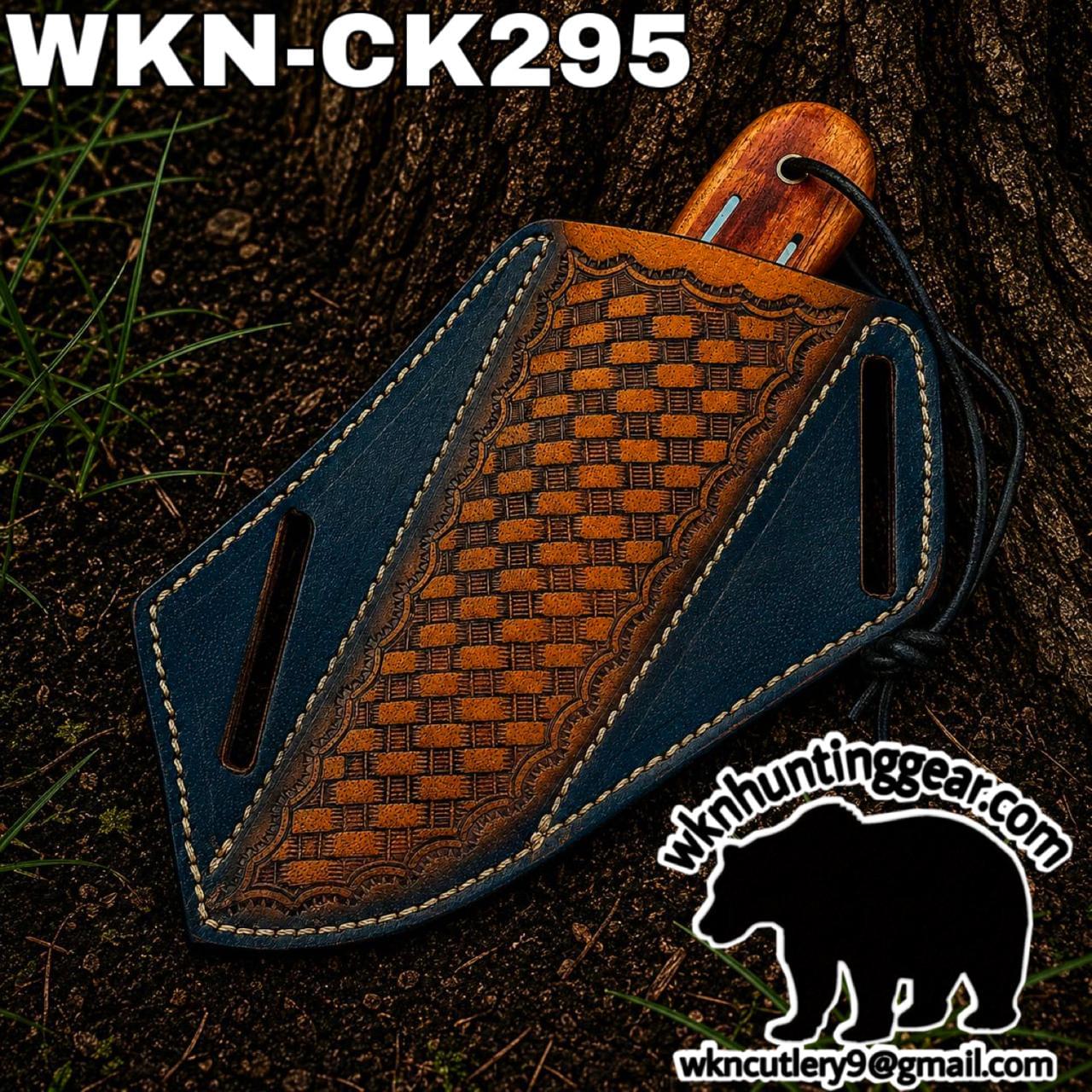 Leather knife sheath with a carved brown center panel and blue edges, wooden handle visible, lying on dirt by a tree.