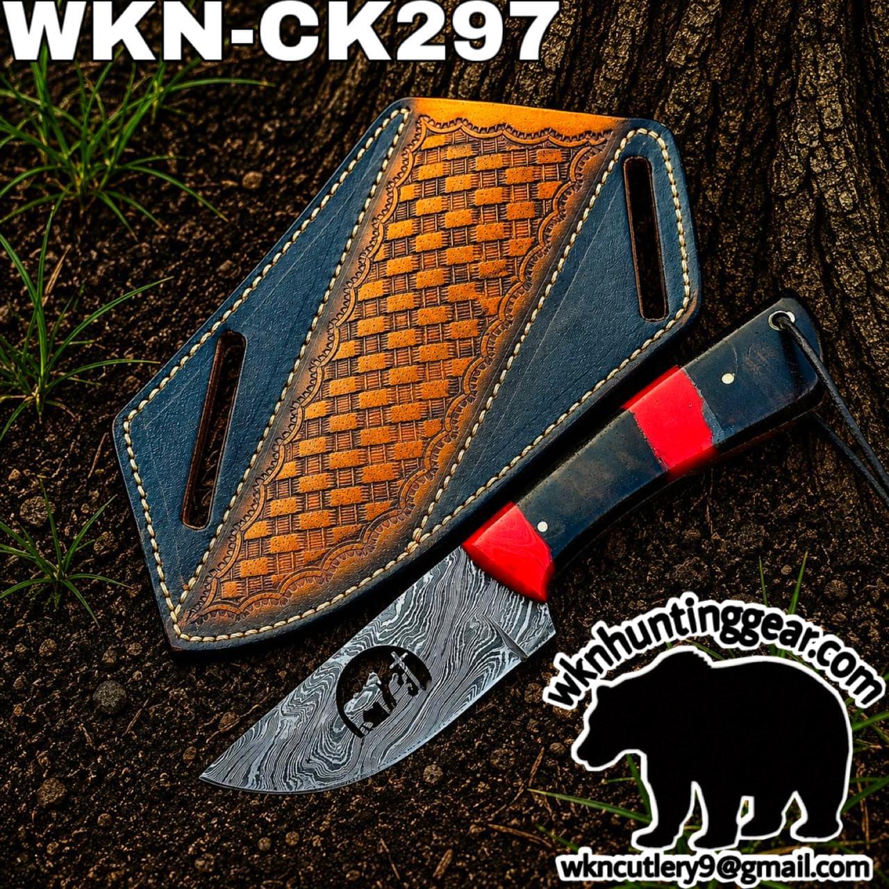 Damascus-pattern hunting knife with red spacer next to a blue leather sheath on dirt, outdoor setting with watermark text in the corner.