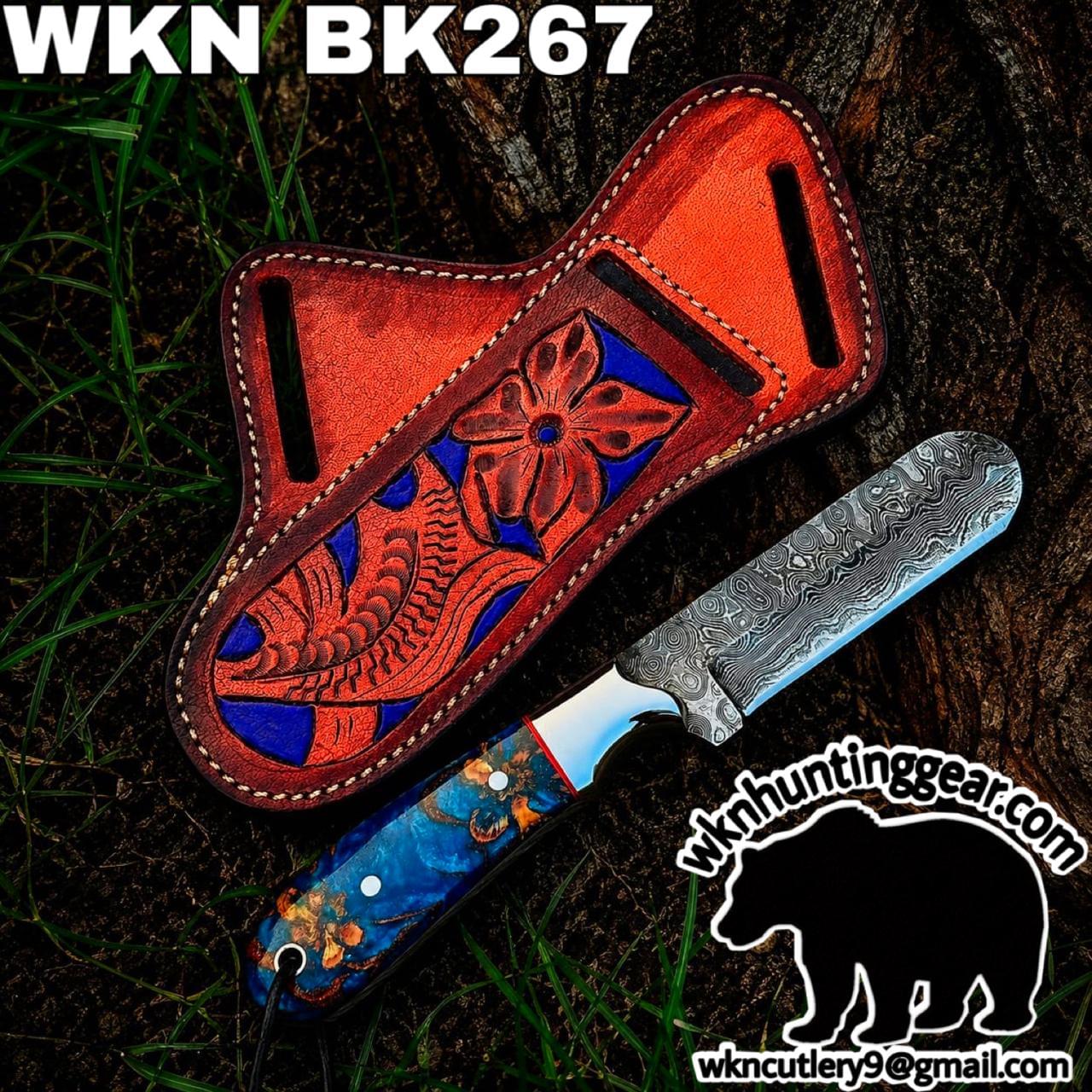 Damascus blade knife with blue floral handle beside an orange leather sheath on a tree stump; watermark for wknc hunting gear in the corner.