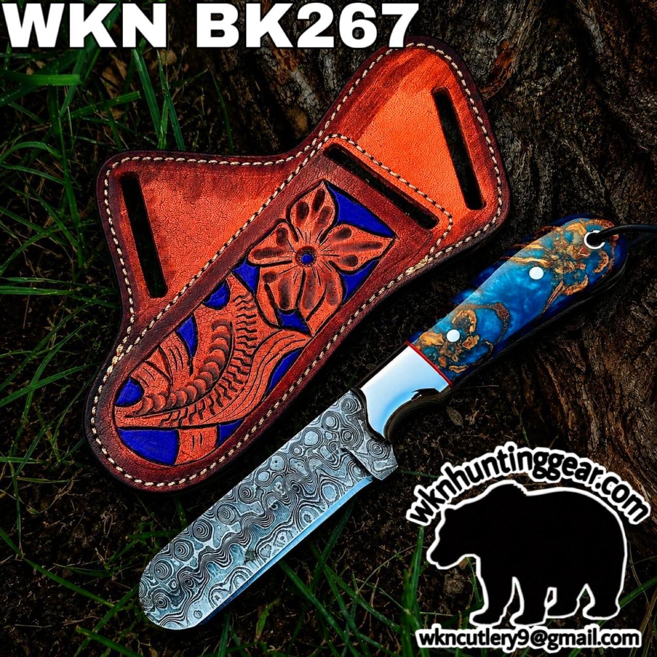 Colorful carving knife with a patterned blade beside a brown tooled leather sheath on grass, branded with WKN hunting gear.