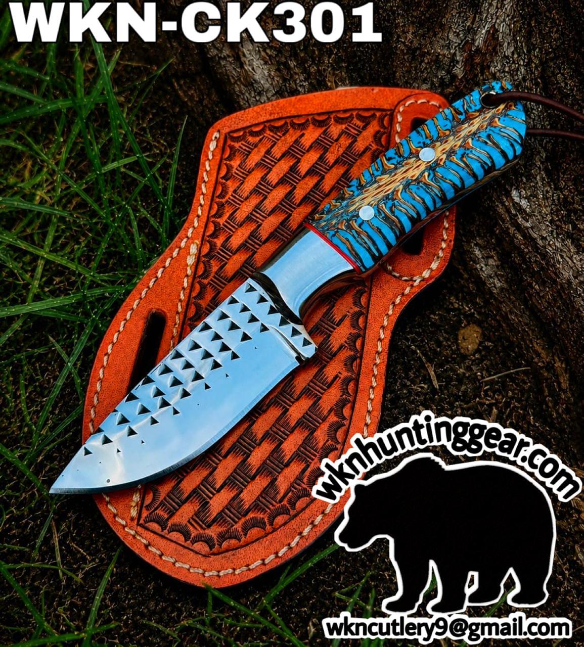 Fixed-blade knife with a blue patterned handle in a brown tooled leather sheath, laid on grass and soil.