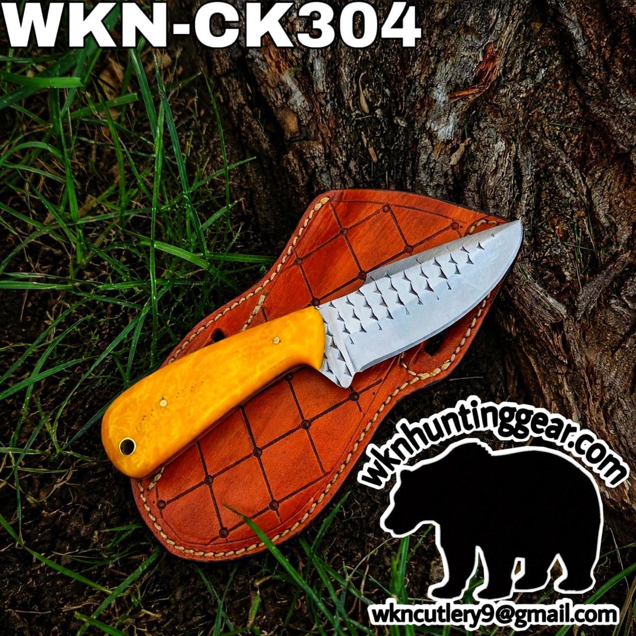 Knife with a bright yellow handle resting on an orange leather sheath beside a tree, part of a wk hunting gear promotional image.