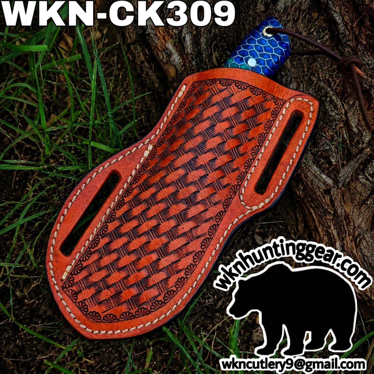 Orange leather knife sheath with a basket-weave pattern and white stitching, lying on grass near a tree trunk.