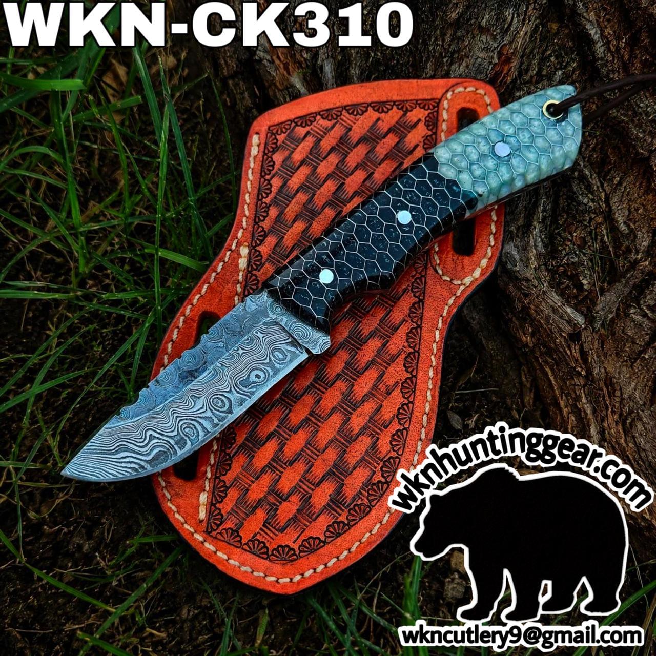 Damascus knife with a patterned blue-green handle laid on an orange leather sheath outdoors by a tree trunk.